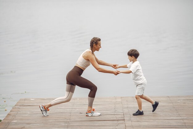 El hijo y la madre están haciendo ejercicios en el parque de verano. Familia junto al agua.