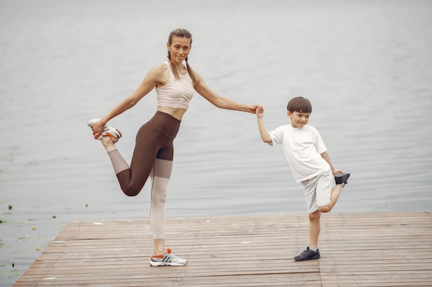 El hijo y la madre están haciendo ejercicios en el parque de verano. Familia junto al agua.