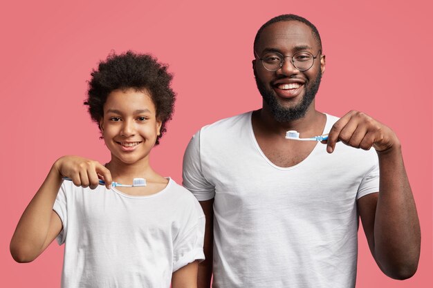 Hijo y padre afroamericano sosteniendo cepillos de dientes