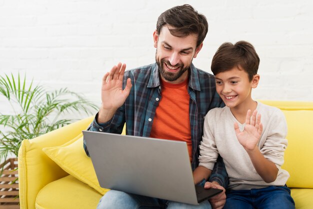 Hijo y padre sosteniendo una laptop y saludando