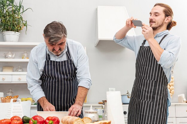 Hijo tomando una foto de su padre cocinando