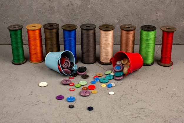 Hilos de coser coloridos junto con botones vintage multicolores de plástico en un gris