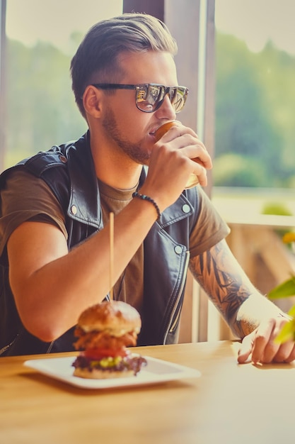 Hipster atractivo vestido con chaqueta de cuero comiendo una hamburguesa vegana.