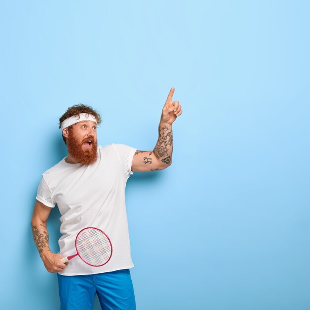 Hipster barbudo en traje deportivo, sostiene raqueta de tenis