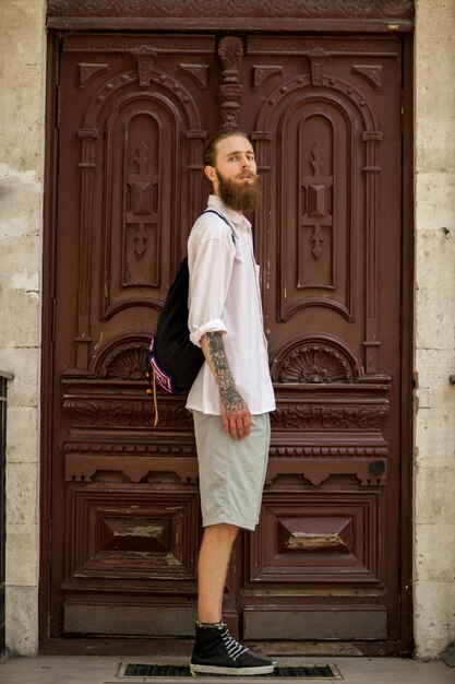 Hipster con camisa blanca posando frente a una puerta afuera de la ciudad. Estilo y diversidad