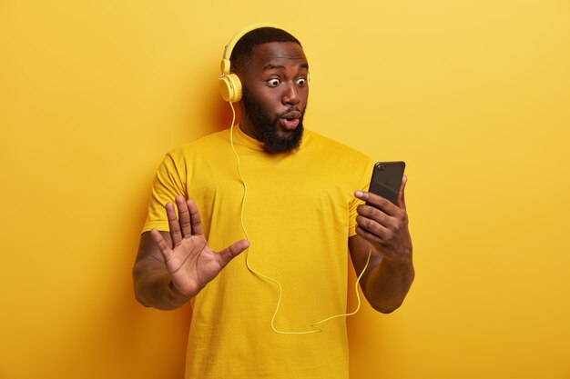 Hipster de hombre negro sorprendido mira fijamente el dispositivo de teléfono inteligente