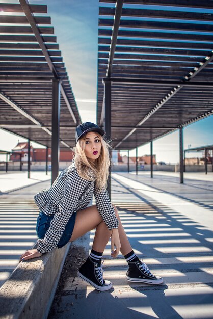 Hipster mujer sentada en el muro de hormigón en un entorno urbano con zapatillas clásicas