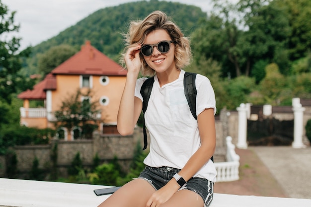 Hipster mujer viajero con mochila en gafas de sol sonriendo y mirando hacia las increíbles montañas y vistas al valle.