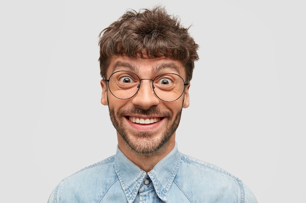 Hipster positivo con barba oscura, tiene una sonrisa suave y sincera, mira con ojos llenos de felicidad