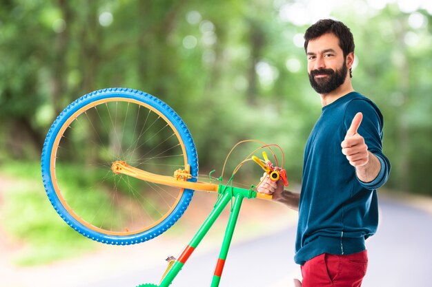 Hipster con el pulgar arriba sosteniendo una bici