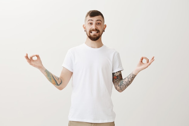 Hipster sonriente alegre con tatuajes meditando, practica yoga