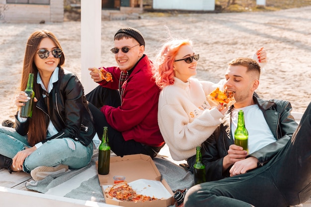 Hipsters jóvenes sonrientes sentados en el suelo con cerveza y pizza