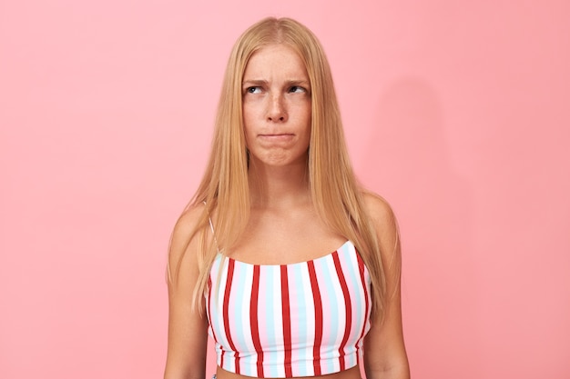 Foto gratuita hmm, déjame pensar. retrato de mujer joven mordiendo los labios, mirando hacia arriba con expresión pensativa, teniendo muchas dudas