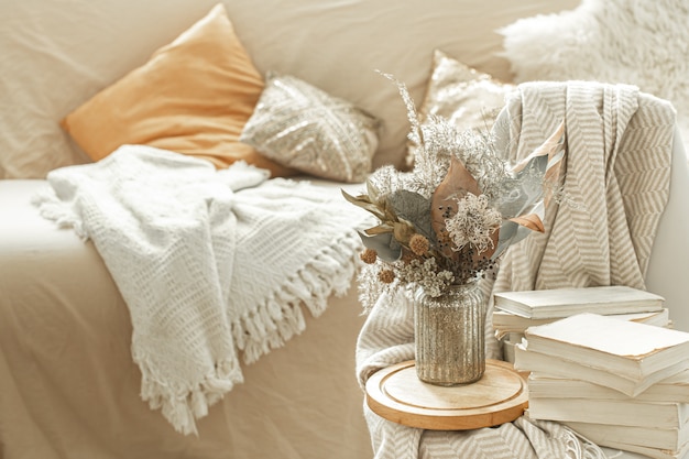 Hogar acogedor interior de la habitación con libros y flores secas en un jarrón.