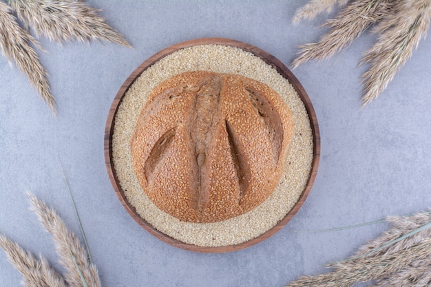 Hogaza de pan en una bandeja llena de semillas de sésamo rodeado con tallos de pasto de plumas secas sobre la superficie de mármol