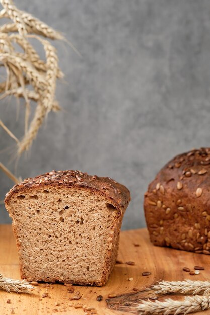 Hogaza de pan de masa fermentada de trigo y centeno con semillas de girasol en una tabla para cortar. Mitades de pan oscuro recién horneado, enfoque selectivo de primer plano. Espigas en la mesa