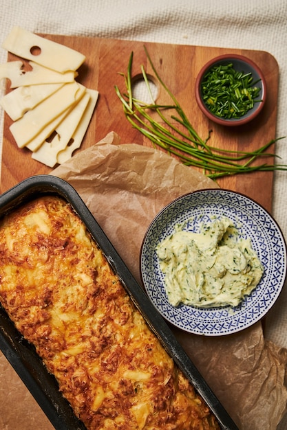 Hogaza de pan de queso con mantequilla de hierbas en una placa de madera con hierbas