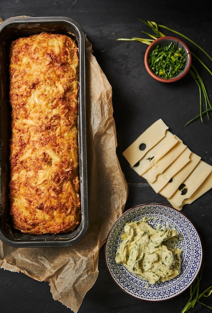 Hogaza de pan de queso con mantequilla de hierbas en una placa de madera con hierbas