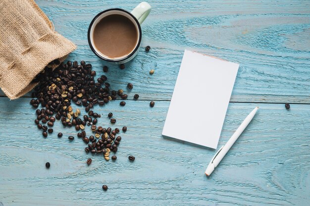 Hoja en blanco; pluma con una taza de café y granos de café en una mesa con textura azul