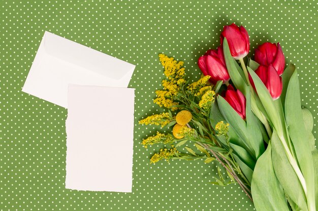 Hoja en blanco; Sobre con flores sobre fondo verde en el día de la madre.