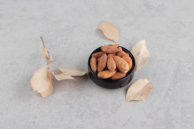 Hoja y un cuenco de almendras, sobre la superficie de mármol