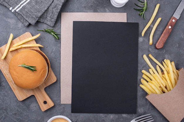 Hoja de papel en blanco al lado de hamburguesas y papas fritas