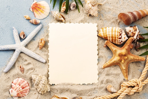 Hoja de papel en blanco con conchas y estrellas de mar en arena