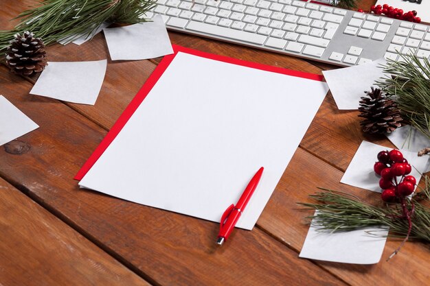 La hoja de papel en blanco sobre la mesa de madera con un bolígrafo y adornos navideños. Concepto de maqueta de Navidad