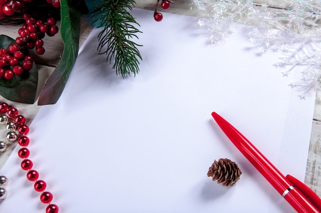 hoja de papel en blanco sobre la mesa de madera con un bolígrafo y adornos navideños.