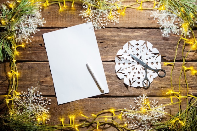 La hoja de papel en blanco sobre la mesa de madera con un bolígrafo y adornos navideños.