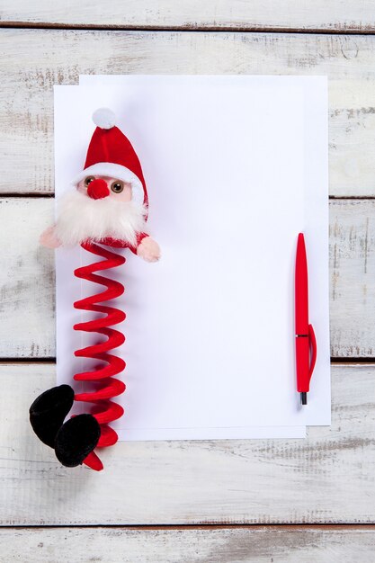 La hoja de papel en blanco sobre la mesa de madera con un lápiz y Santa.