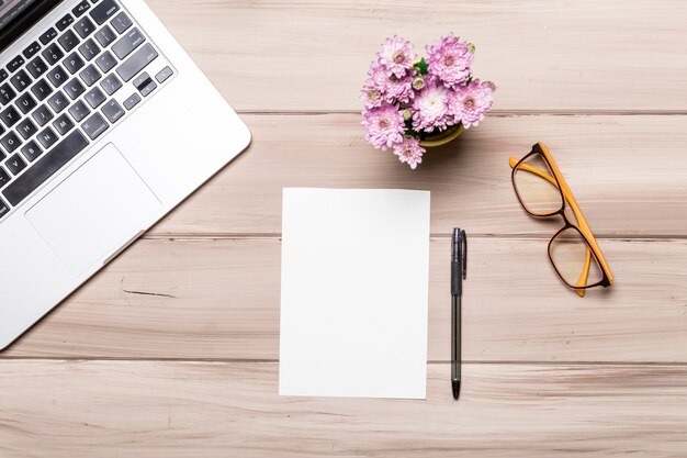 Hoja de papel vacía pluma cuaderno gafas y flores en la mesa