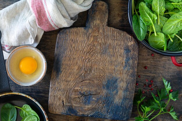 Hojas de espinacas frescas en un bol y huevos en una mesa de madera Vista superior