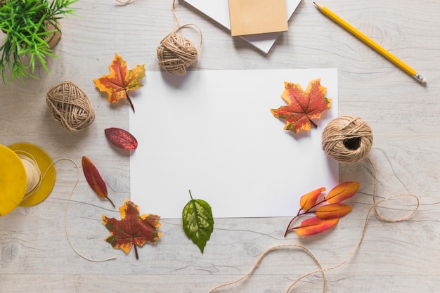 Hojas falsas de otoño sobre papel blanco y cuerda sobre la mesa de madera