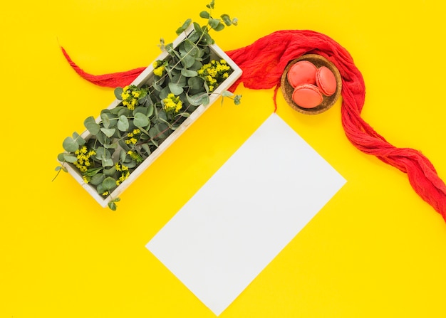 Foto gratuita hojas y flores en la caja de madera; tarjeta en blanco; tazón macarrones sobre fondo amarillo