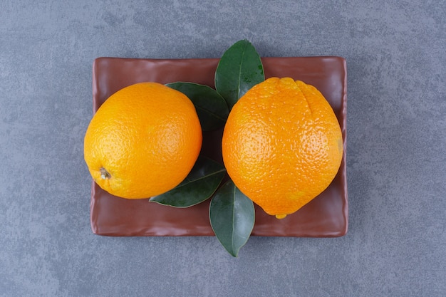 Hojas y naranjas jugosas en placa de madera sobre mesa de mármol.