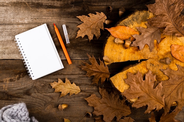 Hojas de otoño y cuaderno sobre fondo de madera