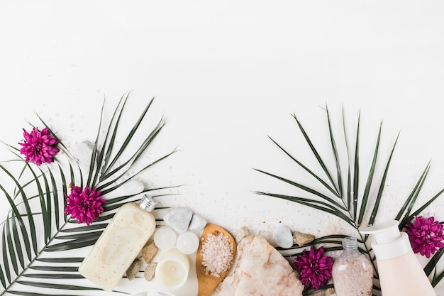 Hojas de palma; flor; exfoliación corporal; sal; piedras de spa sobre fondo blanco