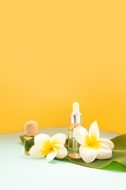 Hojas de palma tropical sobre un fondo de flores Aceite esencial en una botella de vidrio Concepto de spa para cosmética natural y cuidado de la piel