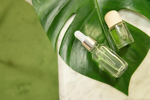 Hojas de palma tropical sobre un fondo de mármol Aceite esencial en una botella de vidrio Concepto de spa para cosmética natural y cuidado de la piel