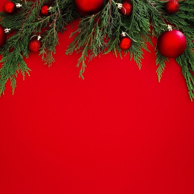 Hojas de pino de Navidad decoradas con bolas rojas sobre fondo rojo con copyspace