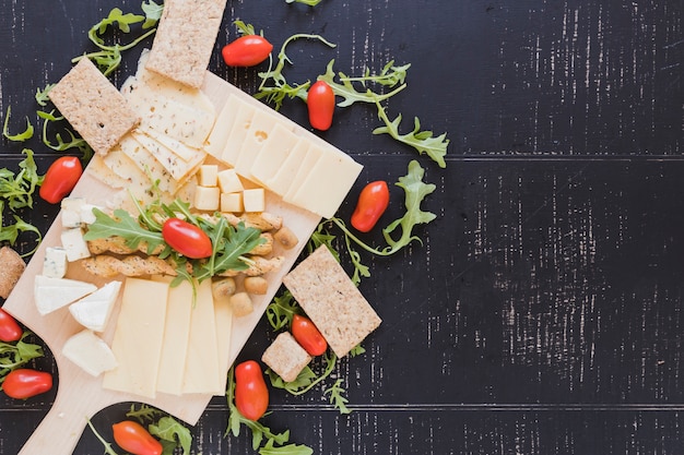 Hojas de rúcula con tomates, queso, palitos de pan y pan crujiente sobre fondo negro con textura