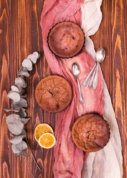 Hojas secas de eucalipto populus y rodajas de cítricos con tres pasteles horneados y cucharas en ropa de lino sobre la mesa de madera