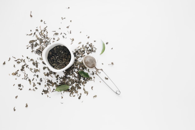 Hojas secas de té con hojas de café y colador de té sobre fondo blanco