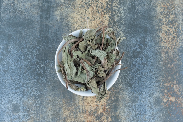 Hojas de té secas naturales en un tazón blanco.