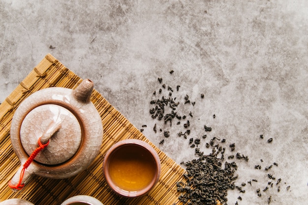 Foto gratuita hojas de té secas con tetera y tazón sobre mantel sobre el fondo de hormigón