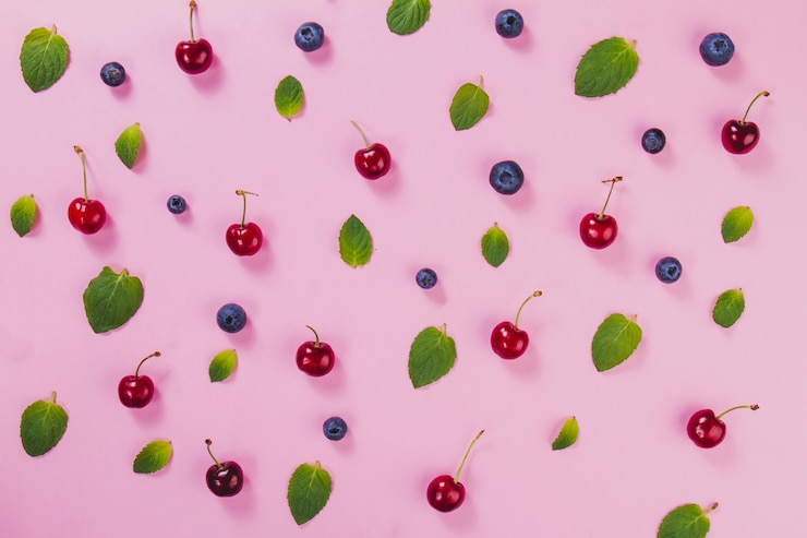 Foto gratuito hojas verdes, cerezas y arándanos sobre superficie rosa