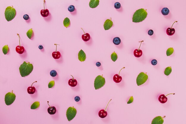 Hojas verdes, cerezas y arándanos sobre superficie rosa