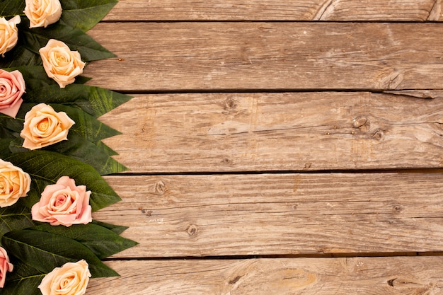 Hojas verdes y rosas sobre fondo de madera con espacio de copia.