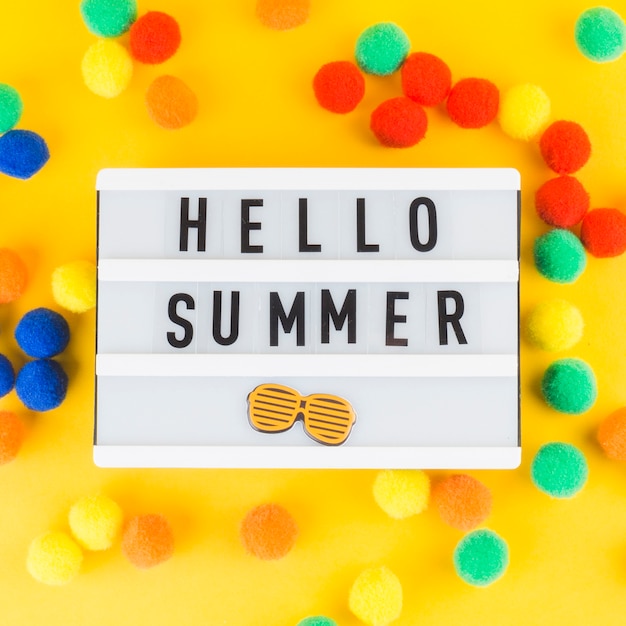 Hola, caja de luz de verano con coloridas bolas pequeñas de pom pom sobre fondo amarillo